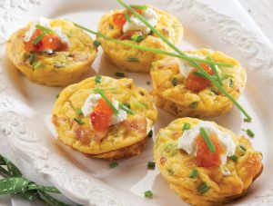 Five frittata muffins on a plate decorated with greens and white cream on top.
